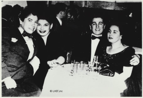 Dos parejas de lesbianas, dos vestidas de hombre, alrededor de una mesa en un club. Fotografía en blanco y negro.