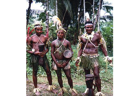 Fotografía de tres miembros de la tribu Sambia en la selva, portando tambores.